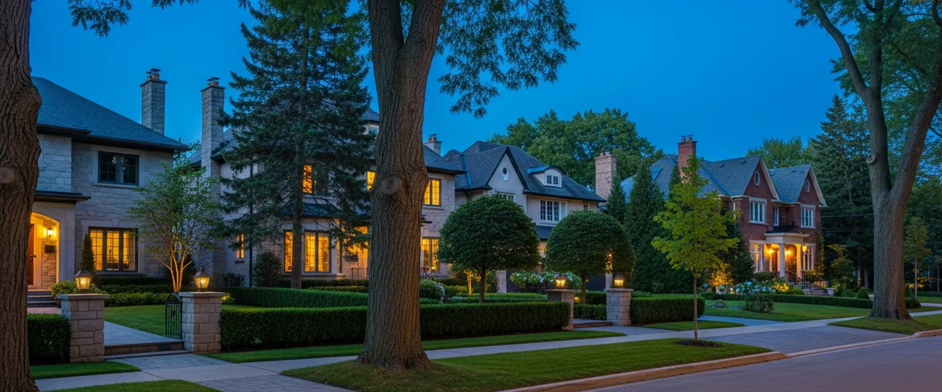 Oakville residential street of established homes on mature lots at dusk with warm window lights against a deep navy sky